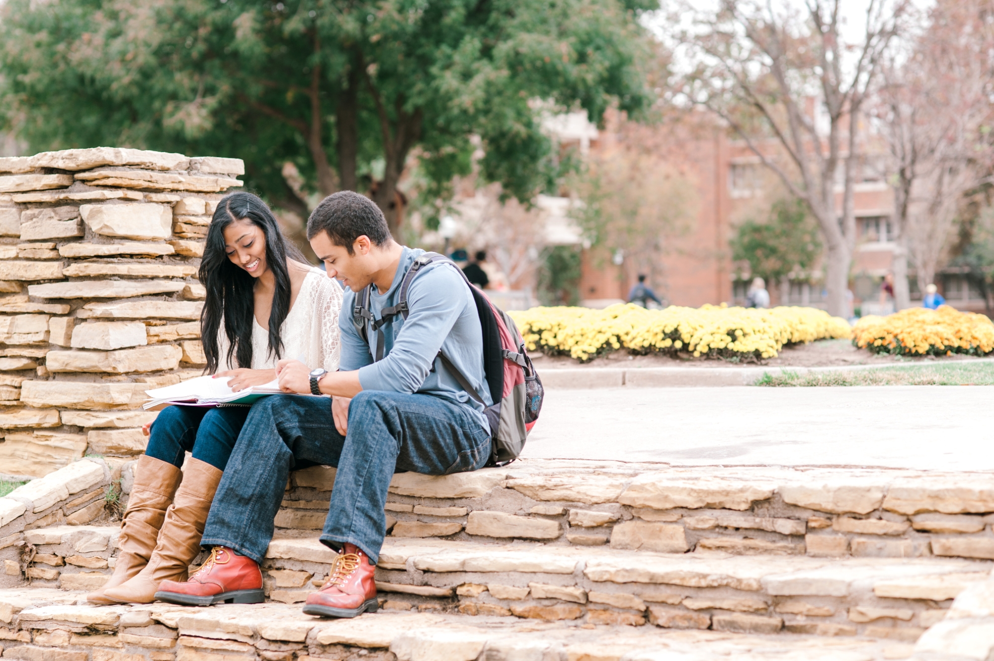 Two students looking at a book and sitting on steps outside. 