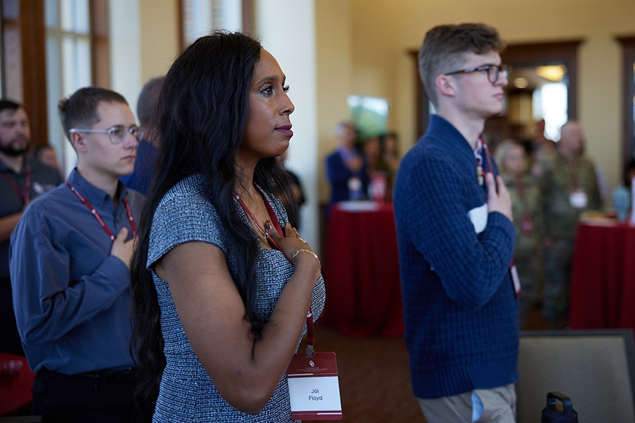 Attendees of the 2024 MVC Reception salute the flag during the National Anthem before the event.