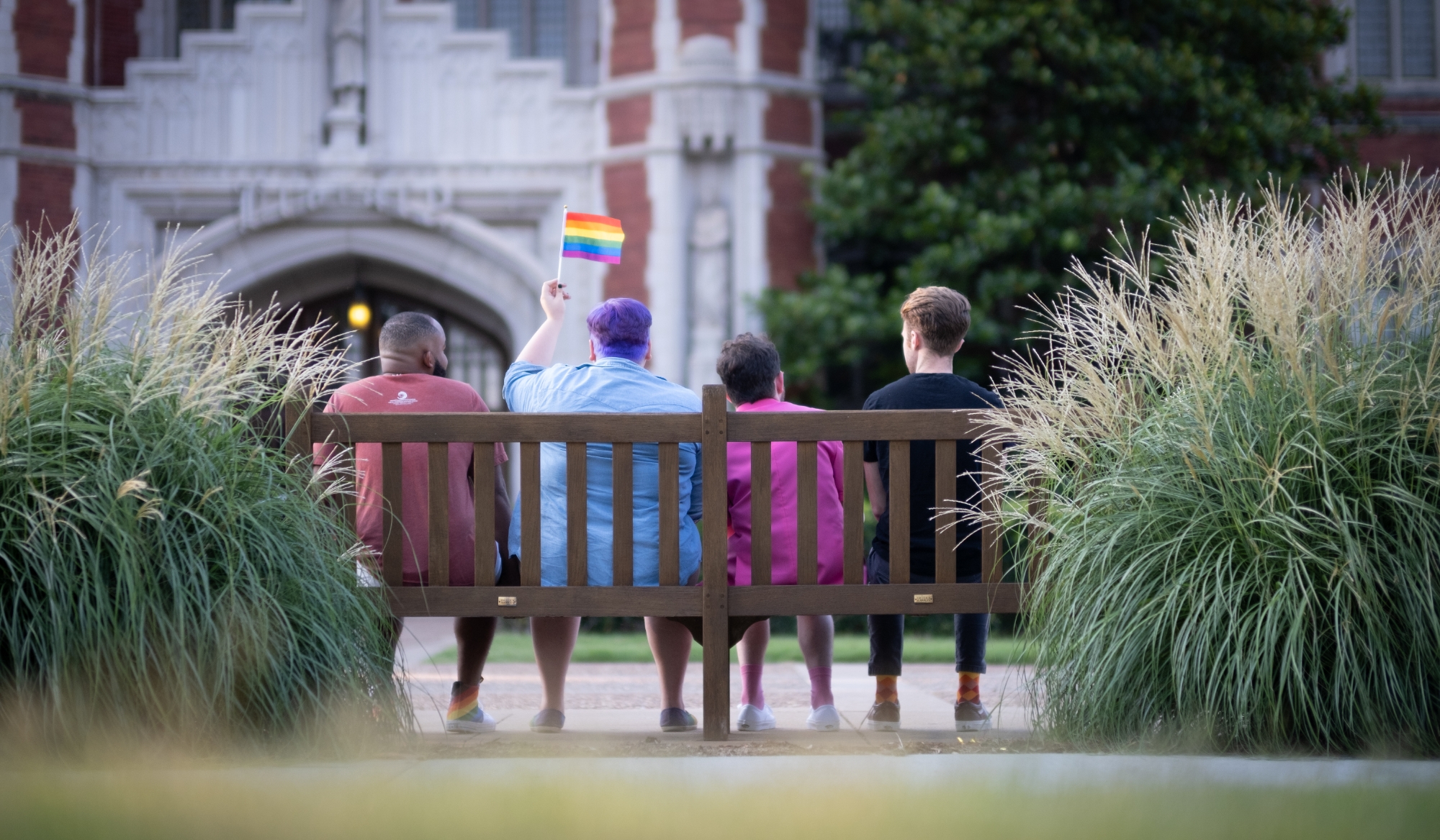 Four Students on Campus; One student holding a pride flag