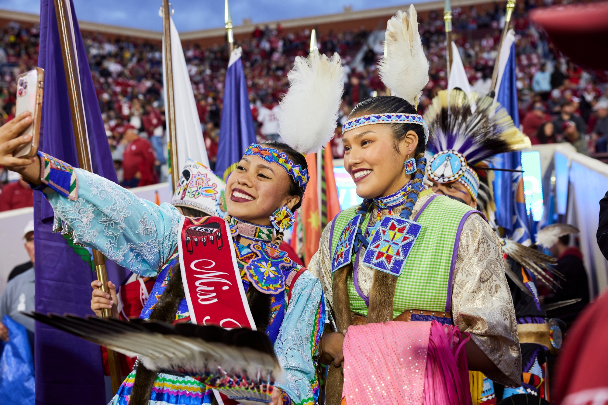 Two students dressed in full regalia taking a selfie while on the football field