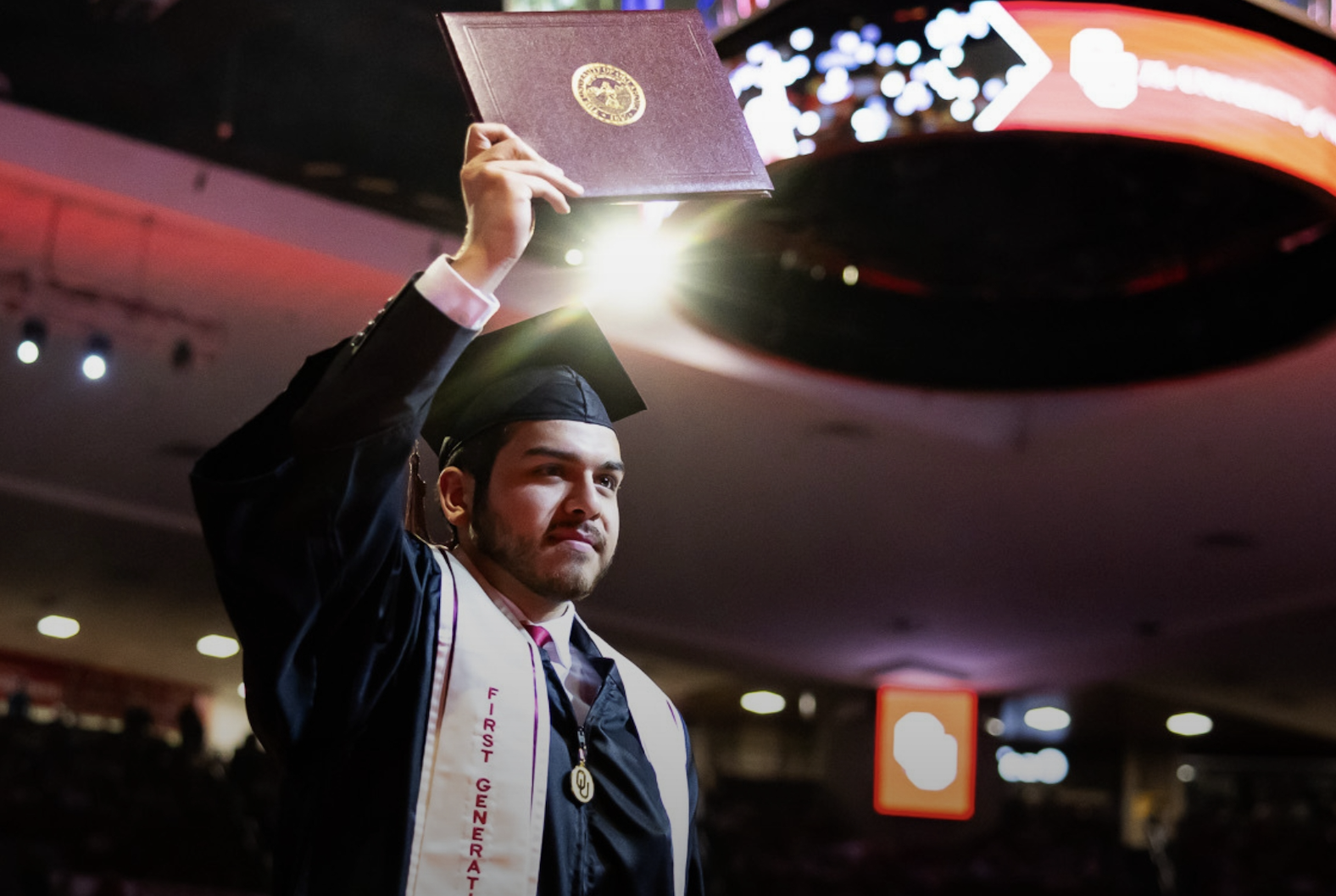 First-generation OU graduate holding up his diploma during graduation. 