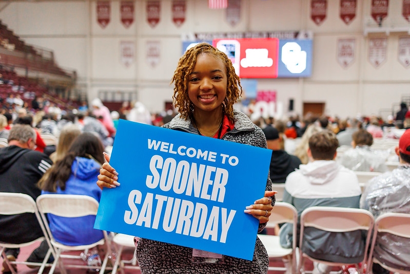 Student holding "Welcome to Sooner Saturday" sign