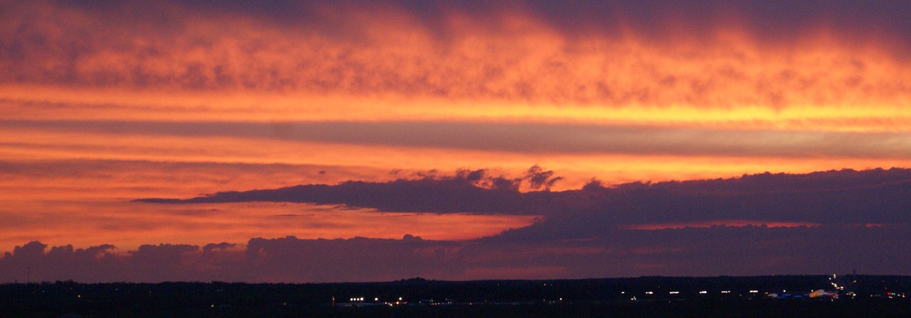 An orange sunset with purple clouds over a dark landscape.
