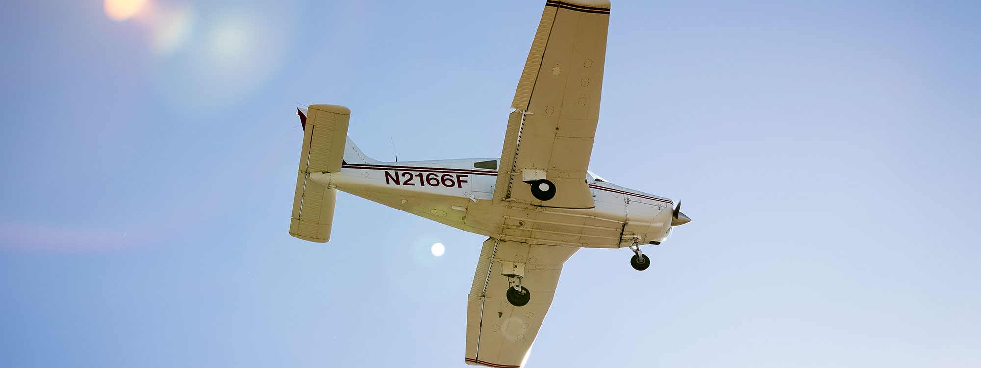 The underside of an airplane flying in the sky with "N 2 1 6 6 F" on the side.