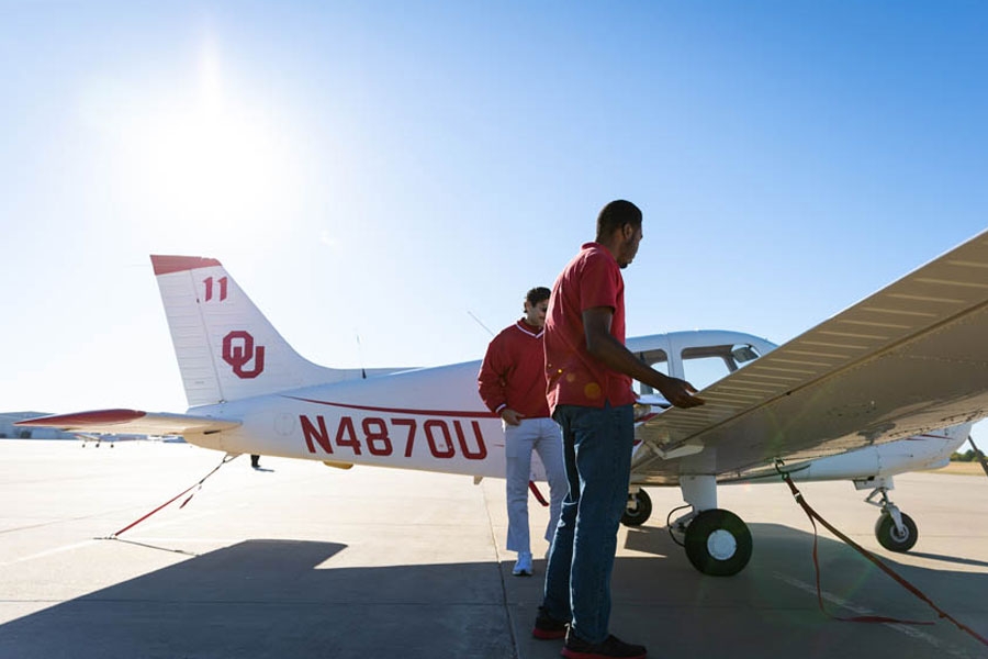 Two aviation students working on the wing of an airplane.