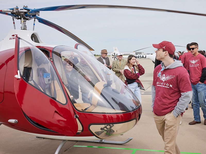 People walking around a crimson helicopter.