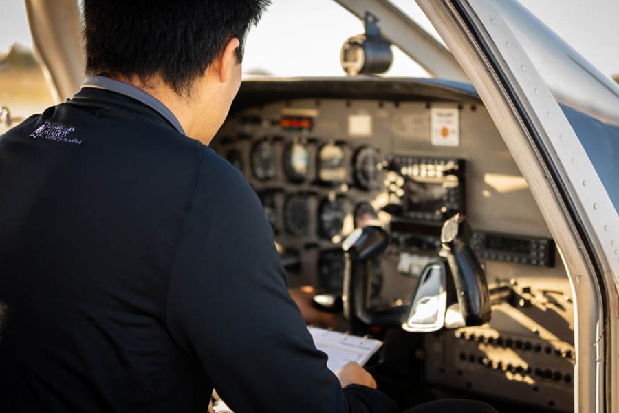 An aviation student holding a clipboard and inspecting a cockpit console.