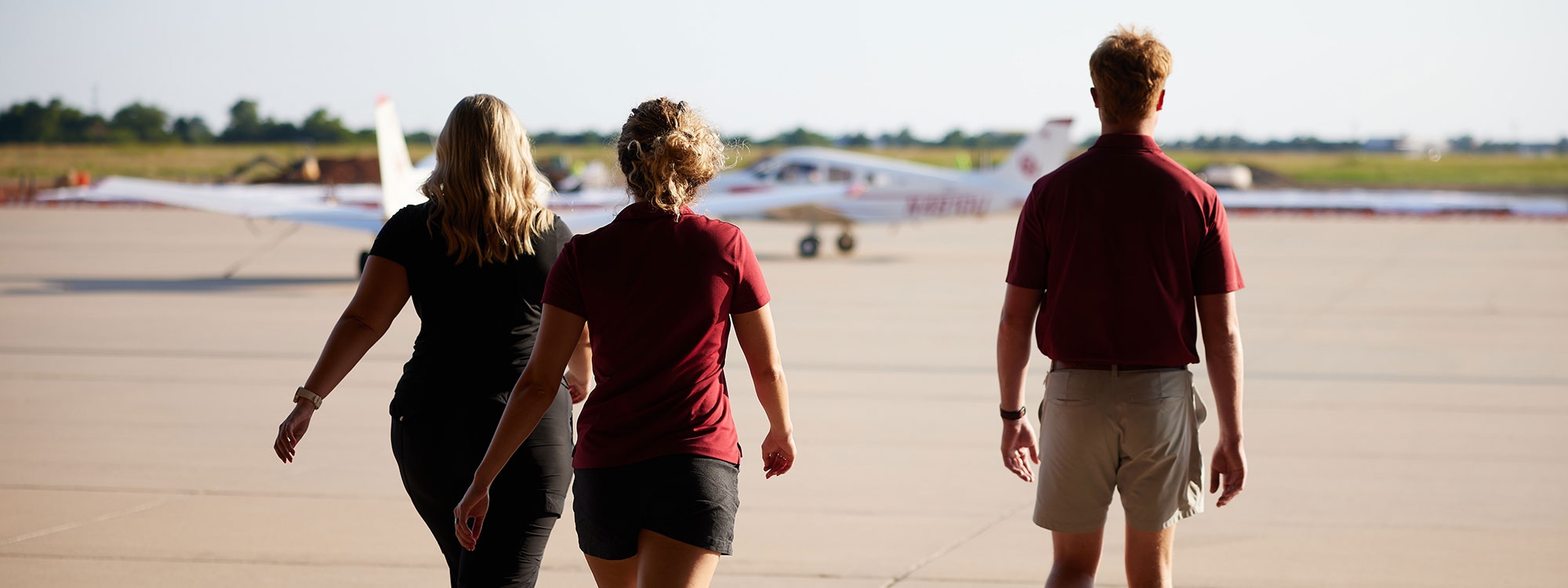 Three students walking towards aircraft on a runway.