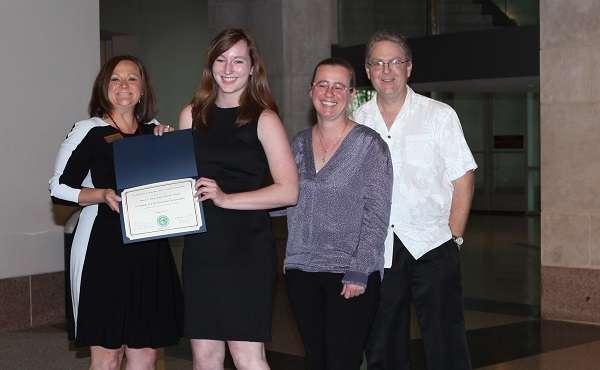 Student at award ceremony holding certificate with Scott Greene and Jamie Steele.