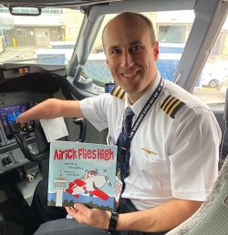 Eric Gaffney sitting in a cockpit of a plane holding a children's book "Airick Flies High" Written by Eric Gaffney