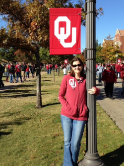 Stephanie Buway wears an OU hoodie, holding onto a lamp post, an OU banner hanging over her head. OU