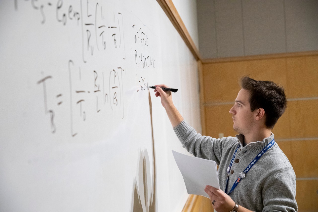 An instructor  displays a calculus equation related to thermodynamics on a whiteboard in a classroom in the National Weather Center.