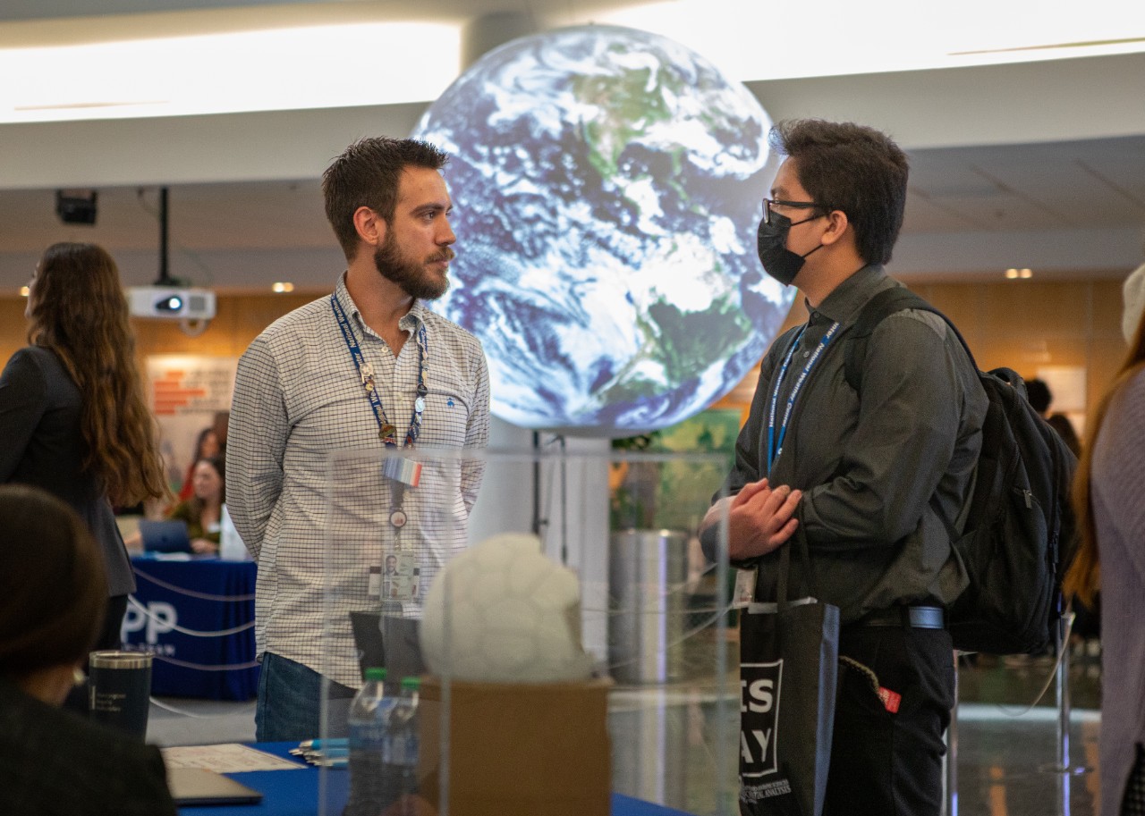 Two men standing in front of the 'Science on the Sphere' globe of Earth at the 2023 A&GS Career and Internship Fair