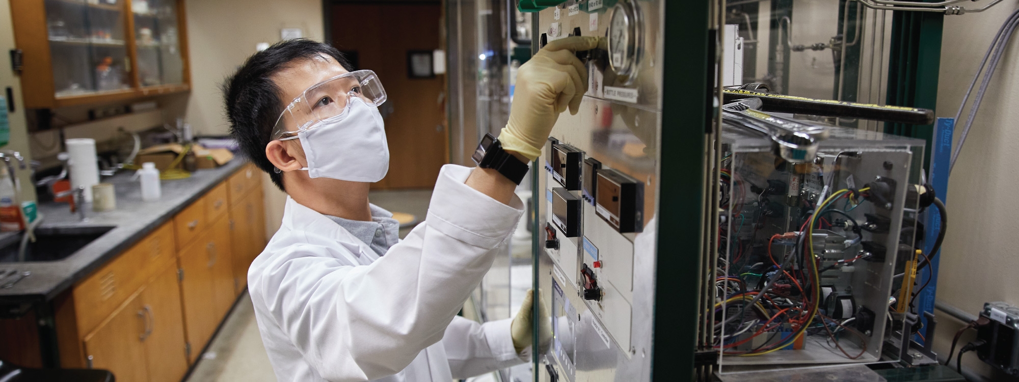A person in a laboratory in protective gear, working with a machine.