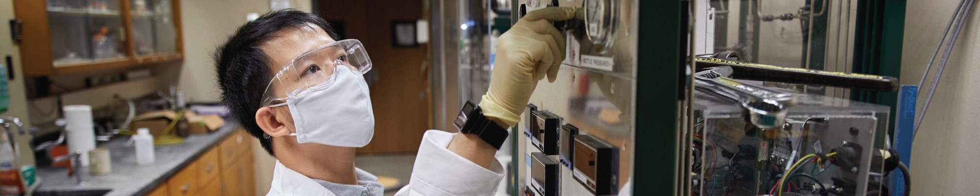 A person in a laboratory in protective gear, working with a machine.