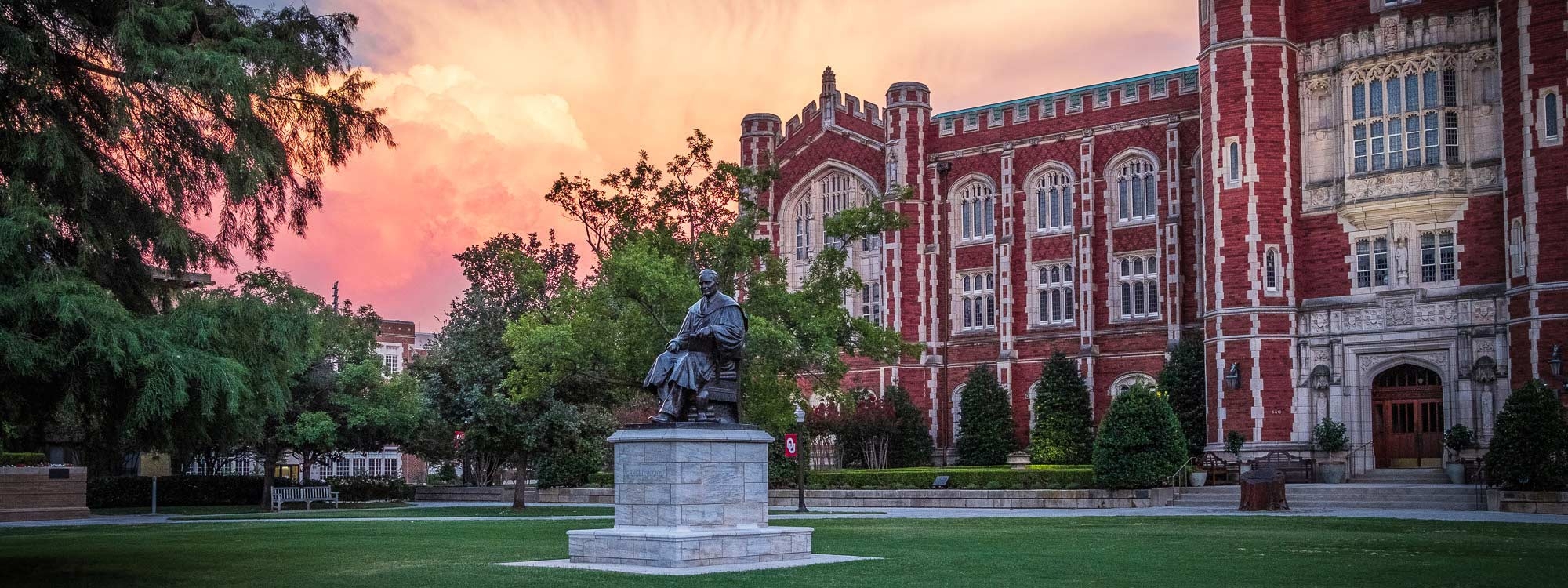 Statue of a scholar sitting in a chair in front of Evans Hall during a cloudy sunset.