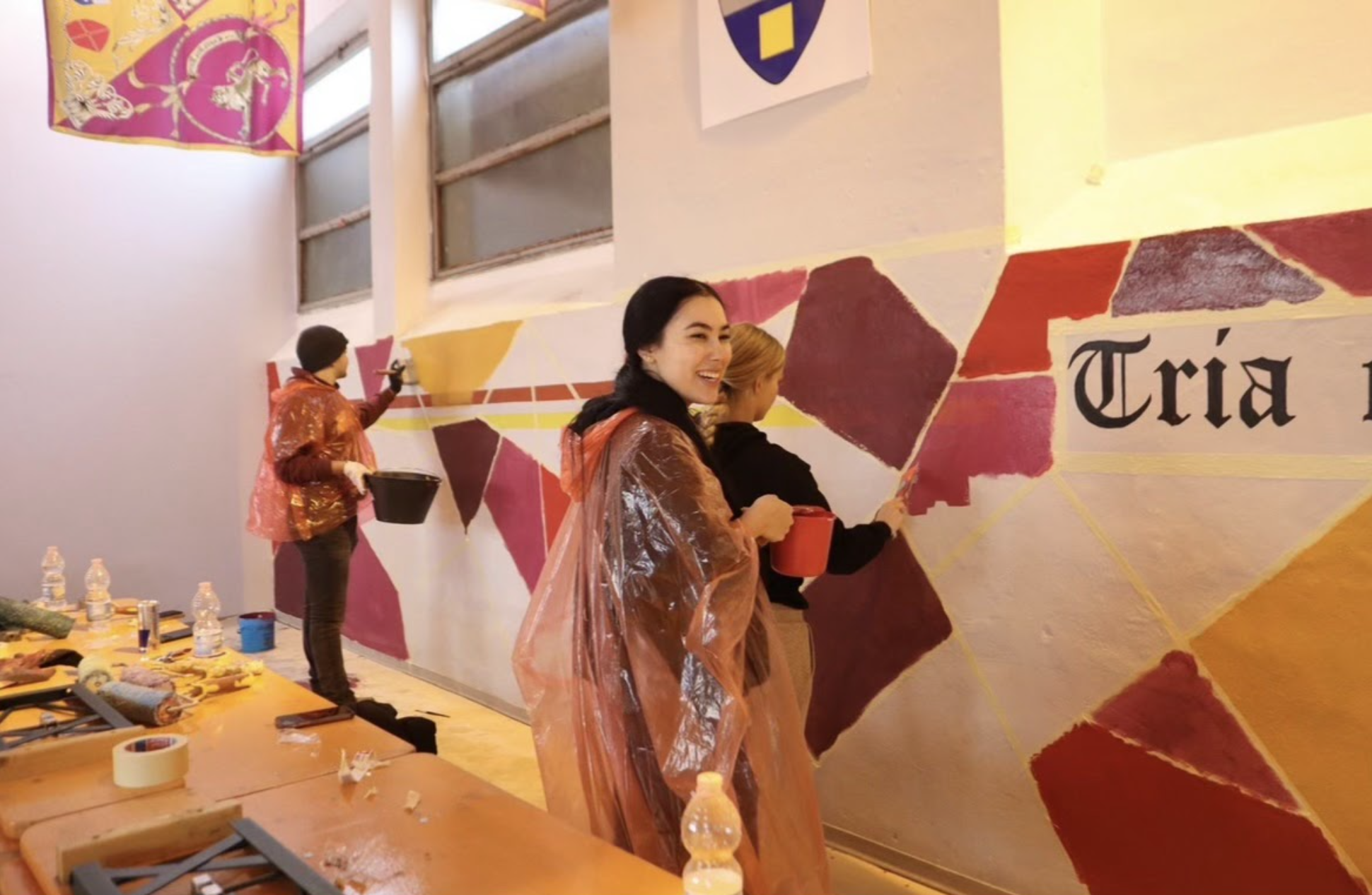 Two students paint a wall with paint rollers while volunteering at The Big Event.