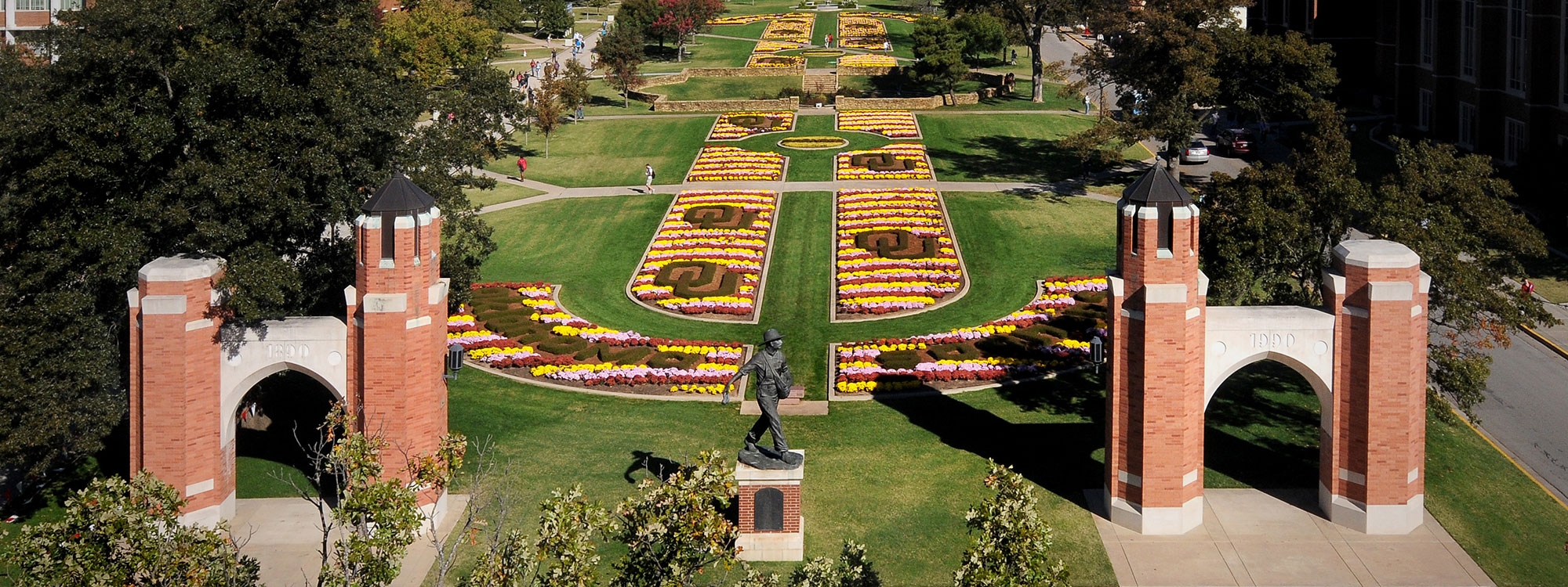 Aerial view of the South Oval, with trees, mums, arches, and the Seed Sower statue and "Oklahoma" and "OU" spelled out in shrubs.