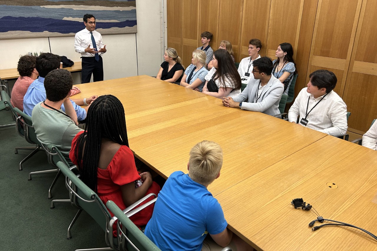 A group of people around a table listening to a speaker. 