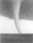 A tornado moving across an open field in black and white.