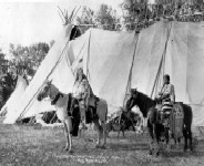 Two Indigenous people on horses in ceremonial clothing, in black and white.