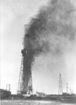 A oil well spewing oil into the air in black and white.