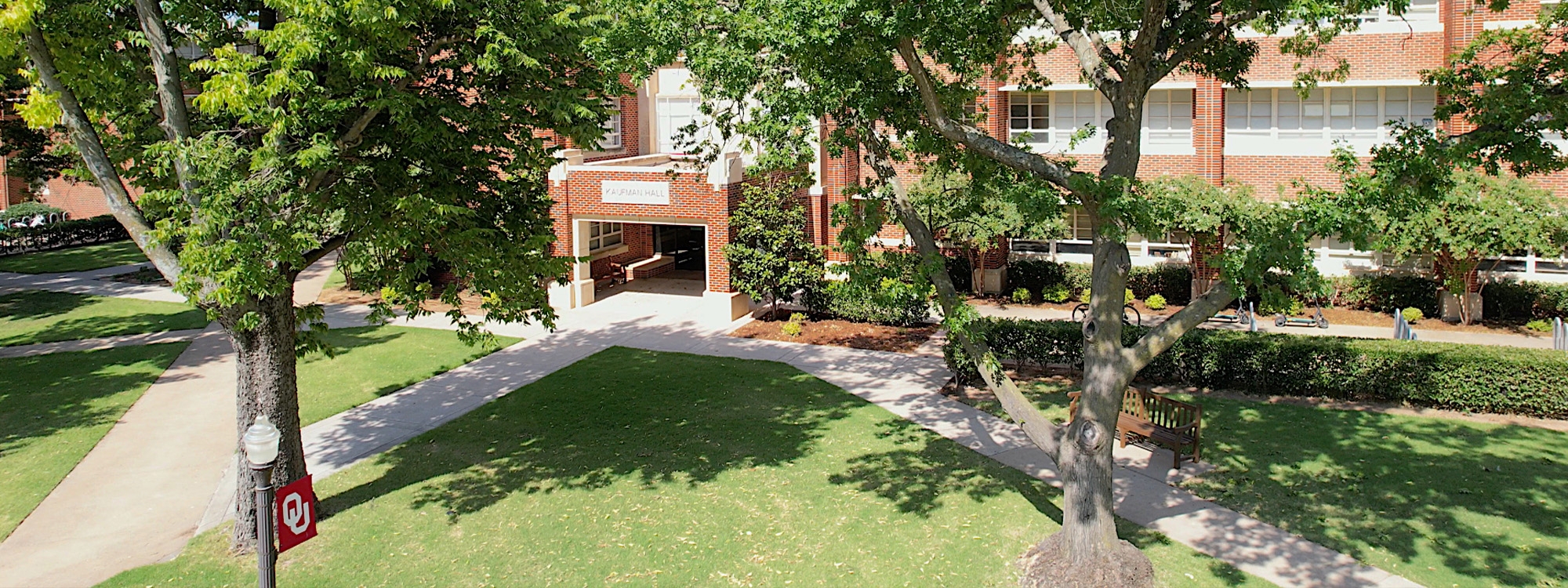 Kaufman Hall, with trees, grass, and a lamppost with an OU flag in the foreground.