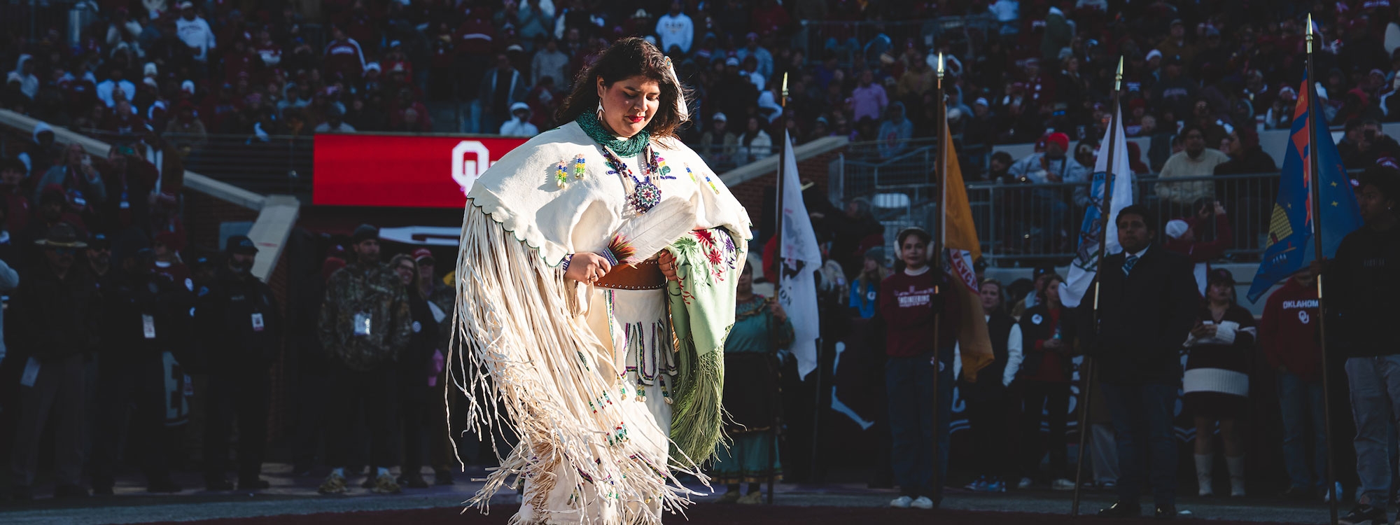 A woman in Native clothing performing a traditional dance at a football game.