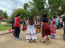 Several students are in a circle, many in traditional Native dress.