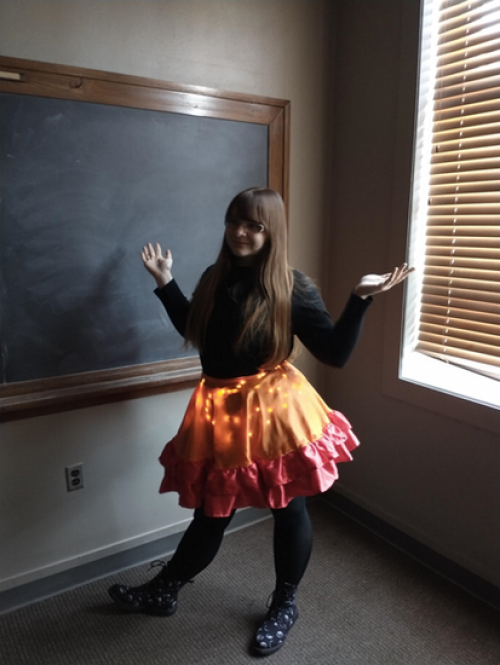 A photo of Shania Wolf wearing a black top, black leggings and shoes, and a red and orange lit dress.