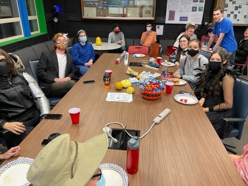 Students in SPS celebrate Halloween in the physics lounge, sitting at a table with candy and other food treats.