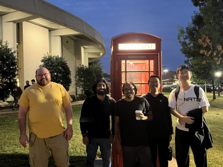 A small group from the High Energy Physics research group standing in front of a phone booth.