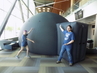 Kyra Dame and Evan Rich posing in front of the black inflatable planetarium.