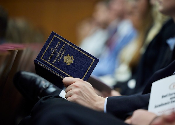 Person holding a booklet with the title, The Constitution of the United States of America.