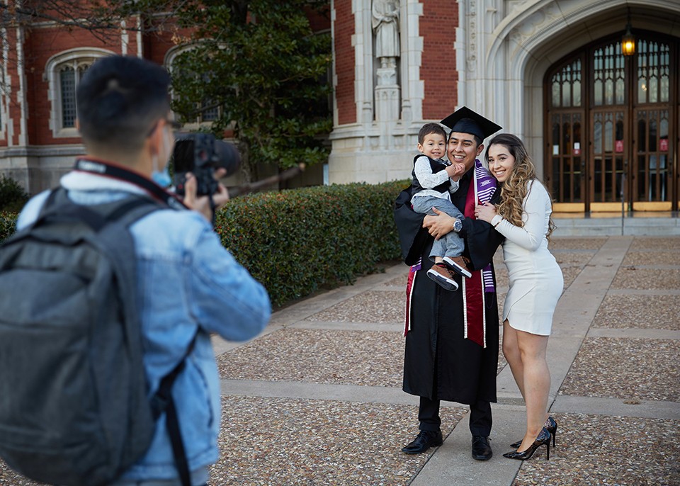 Photographer in foreground taking picture of a graduate and family.