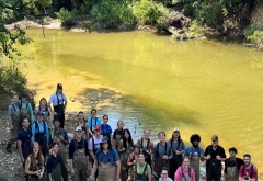 group of students smiling with tools in tall grass 