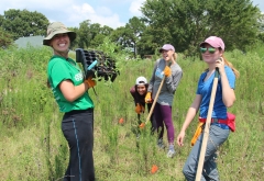group of students smiling with tools in tall grass 