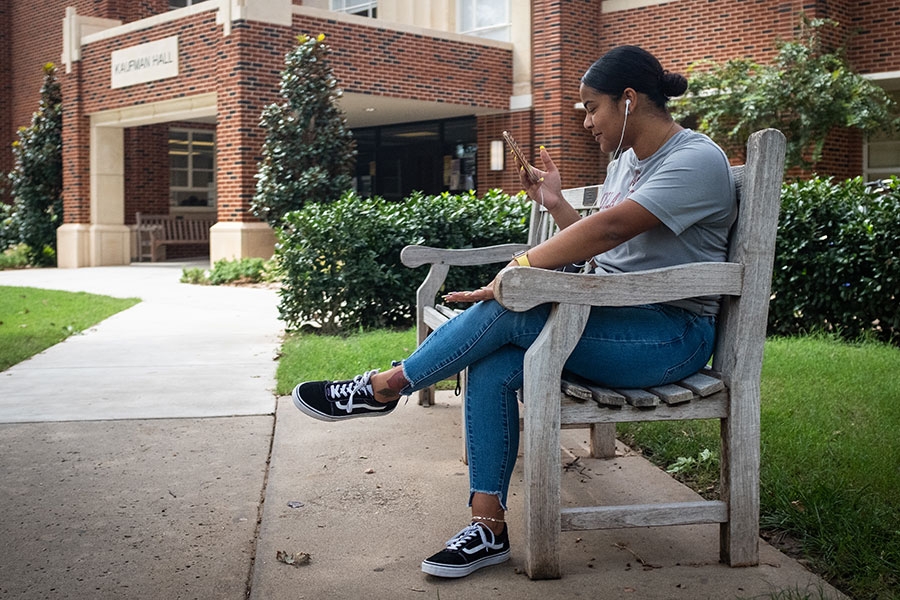A student sitting outside on a bench on a sunny day.