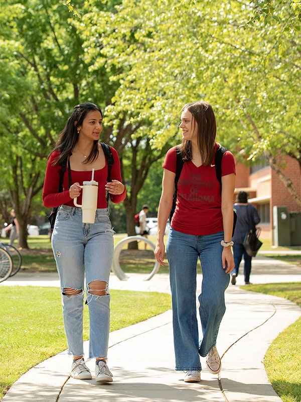 Students walking on a campus sidewalk surrounded by trees.