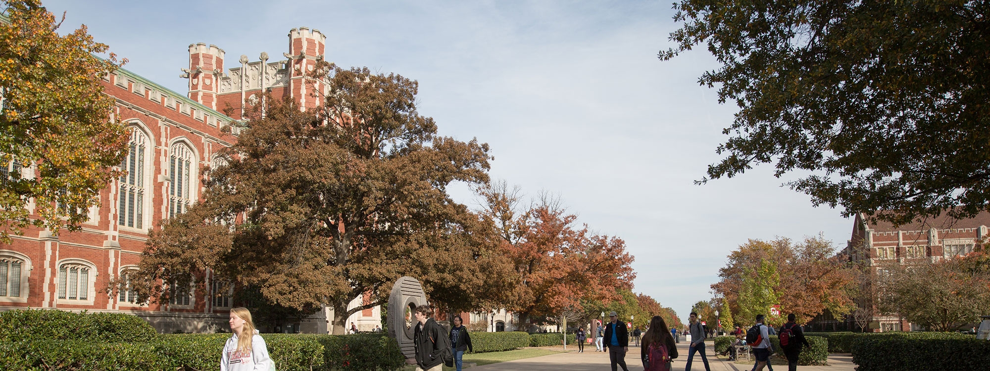 Students walking on the Norman campus on tree lined sidewalks with Bizzell Library in the background.