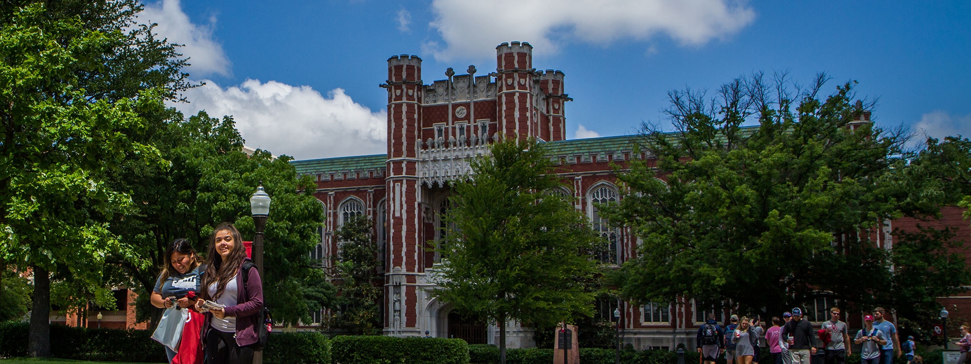 Students walking on the Norman campus on tree lined sidewalks with Bizzell Library in the background.