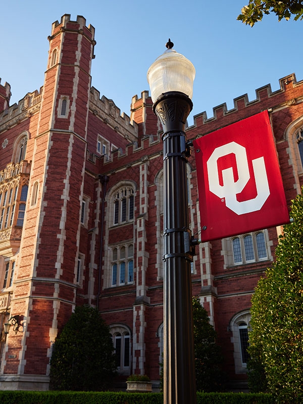 A lamppost with an OU flag in front of the historic entrance of Bizzell Library on the Norman Campus.