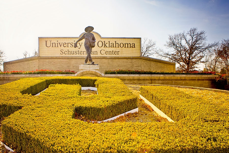 A large OU logo topiary frames a Seed Sower statue on the Tulsa Campus.