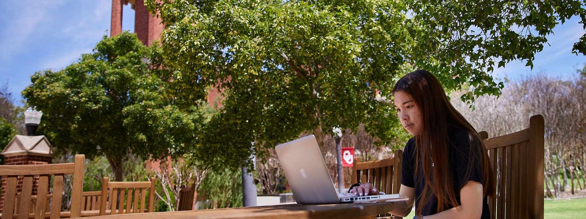 A student sitting at a table outside, working on a laptop.