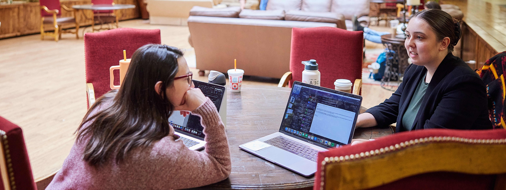 Two students with laptops, sitting at a table.