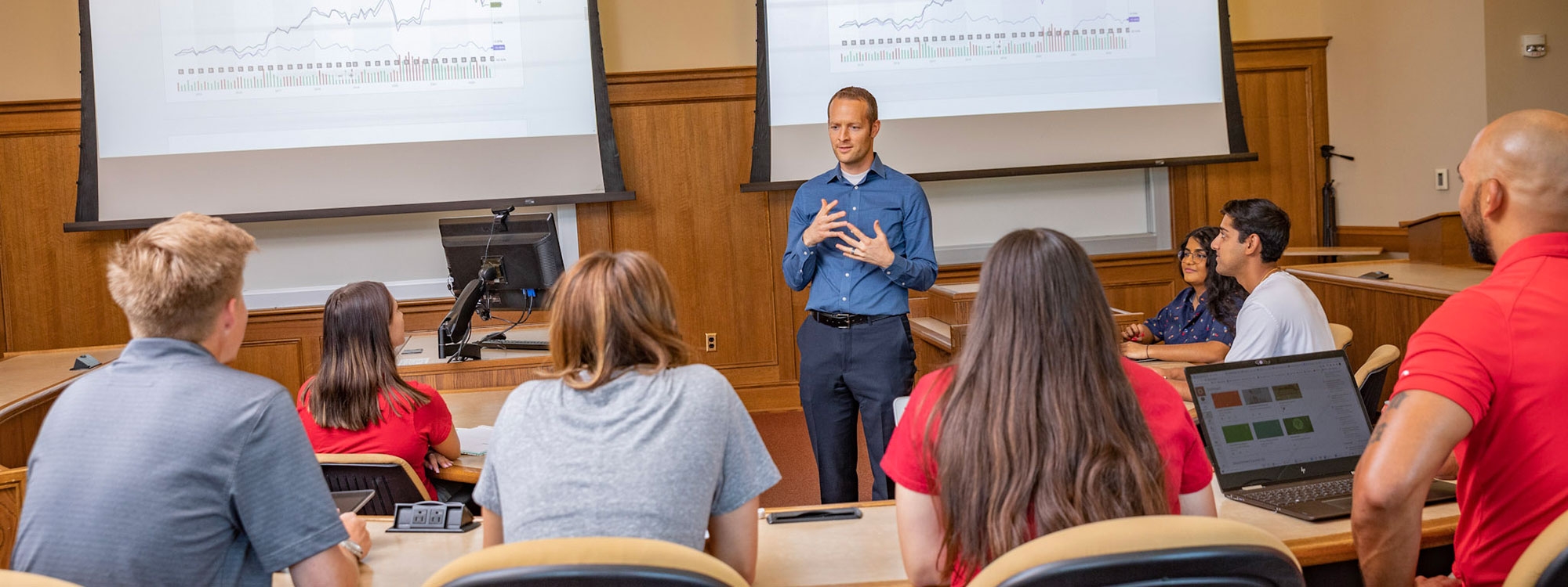 An instructor standing in front of a projection screen, speaking to students.