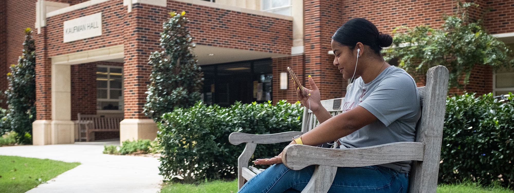 A student sitting on a bench outside Kaufman Hall.