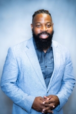 Rodney wears a blue suit and smiles.