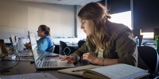 Student at a desk typing on a laptop in a classroom.