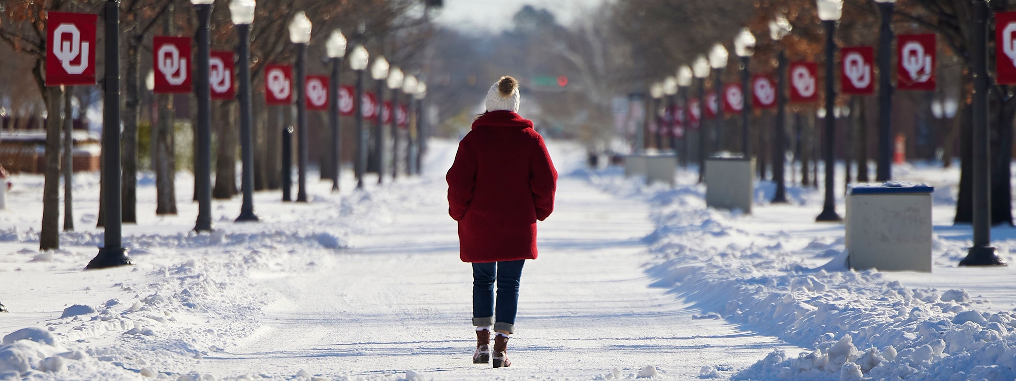Student walking down snow covered path with light poles